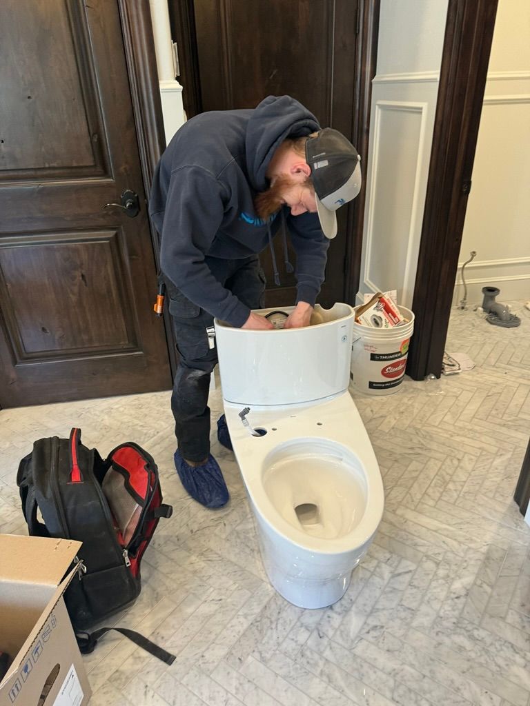 A plumber is working on a toilet in a bathroom in Ogden UT.