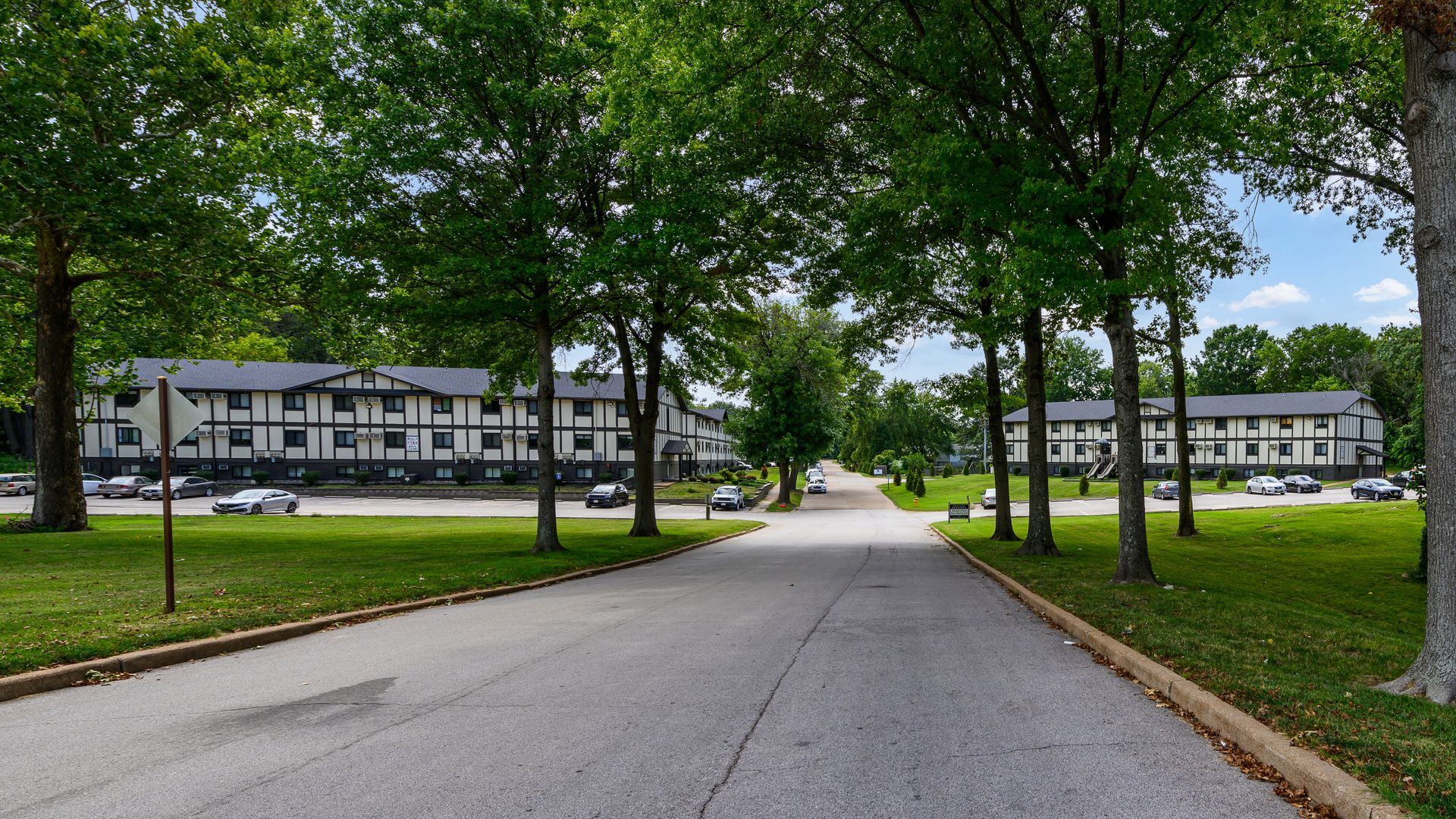 A road leading to a row of buildings surrounded by trees.