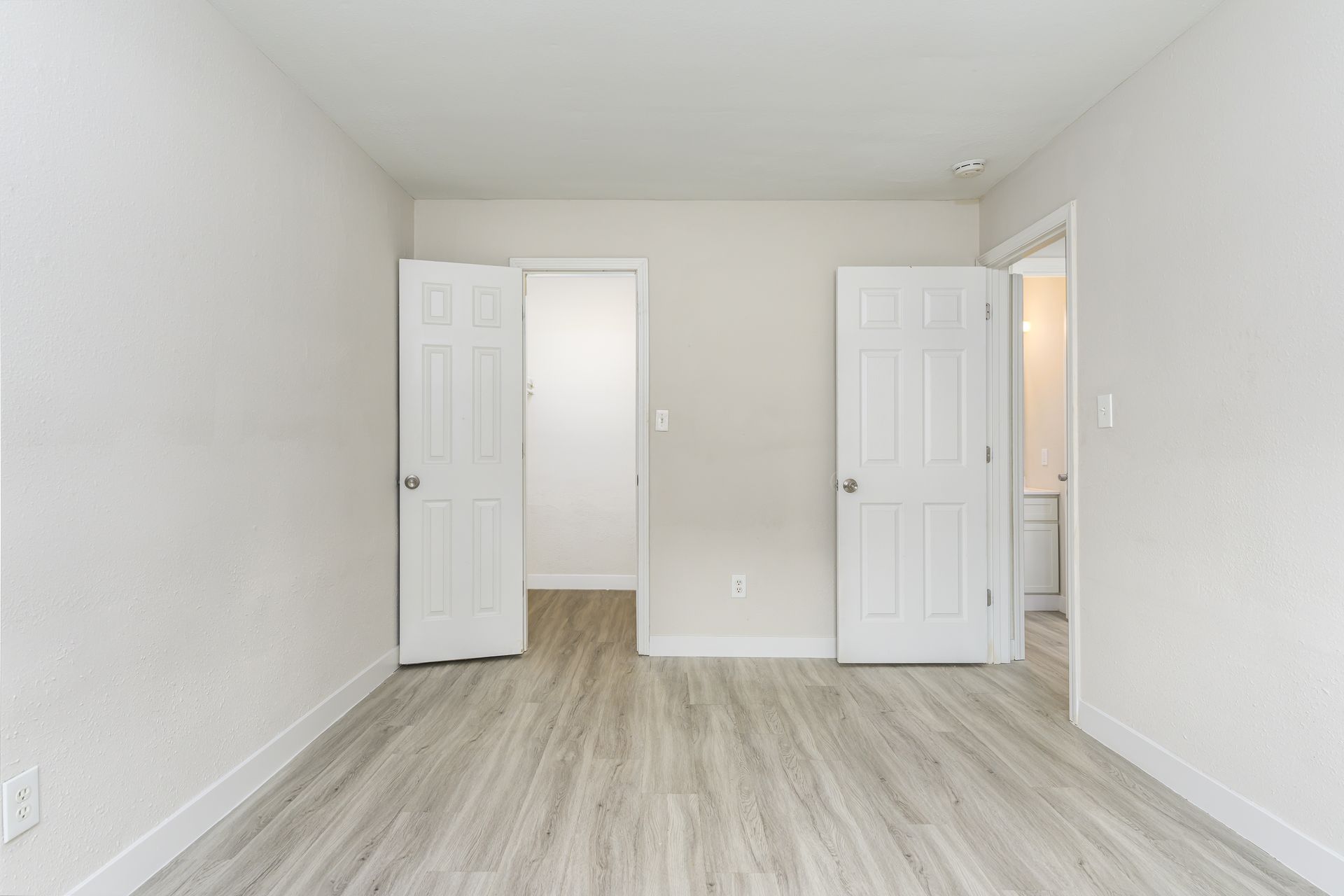 An empty bedroom with hardwood floors and white walls.