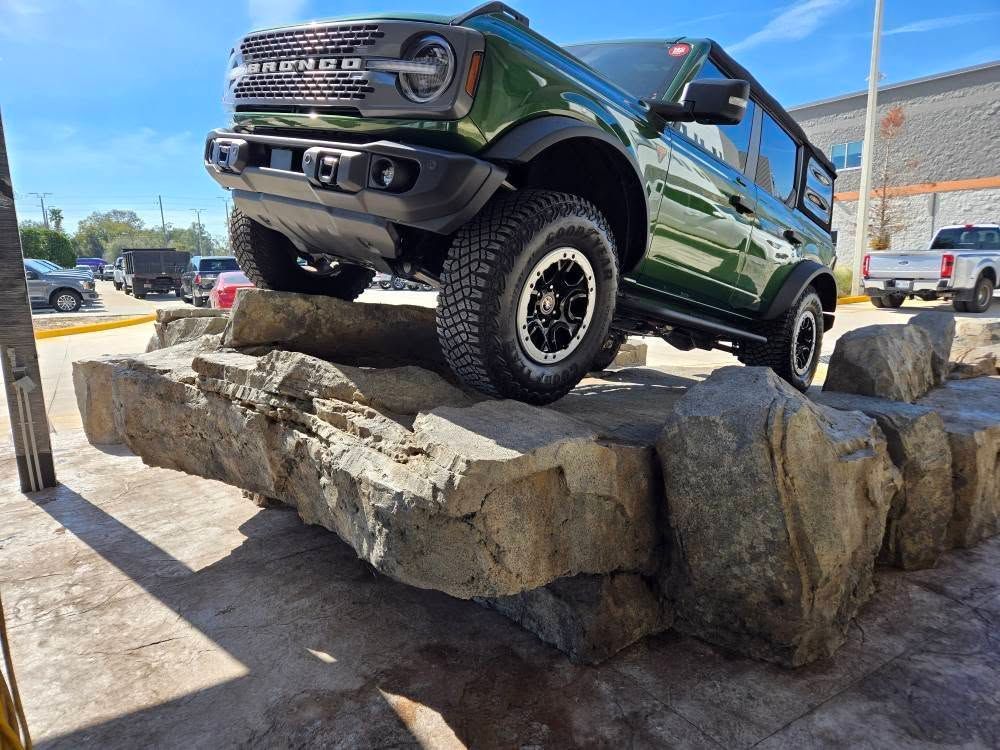 Green Ford Bronco SUV driving over a rock obstacle course on a sunny day.