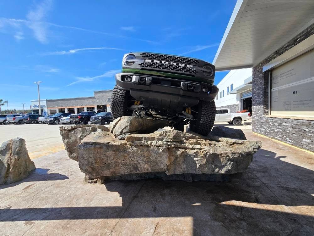 Green Ford Bronco on large rocks, angled, front view, in front of a building on a sunny day.