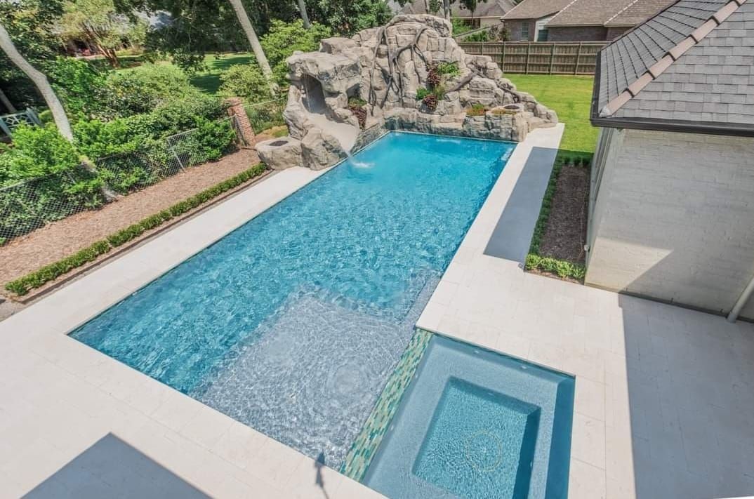 Outdoor rectangular pool with a rock waterfall feature and attached hot tub.