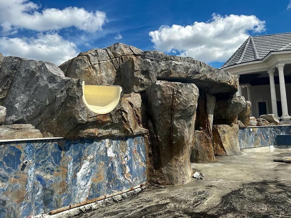 A large rock formation with a yellow waterslide built into it, surrounding an empty swimming pool. Blue sky.