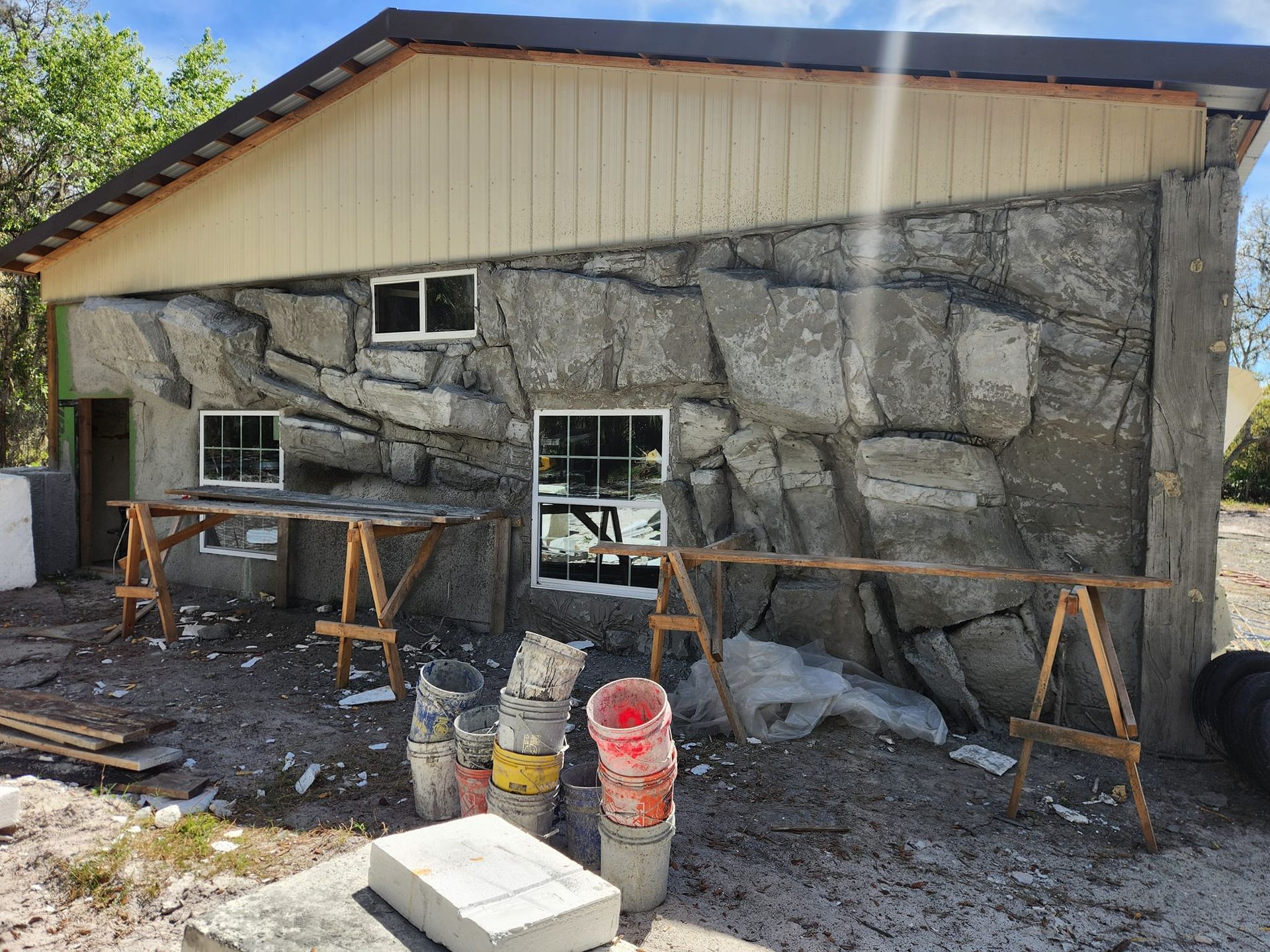 Building exterior with textured, stone-like facade; windows, wooden scaffolding, and construction materials visible.