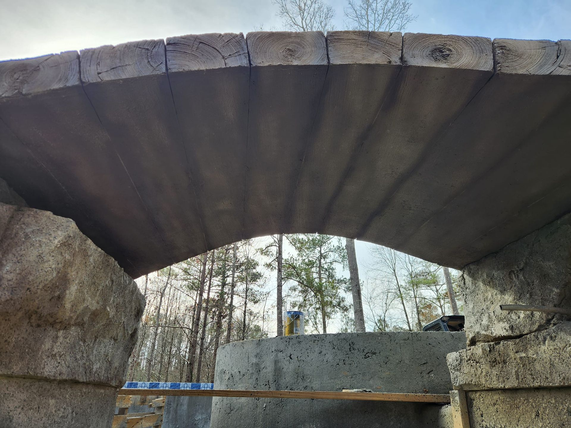 Concrete archway under construction, with wooden beams at the top. Forest in the background.