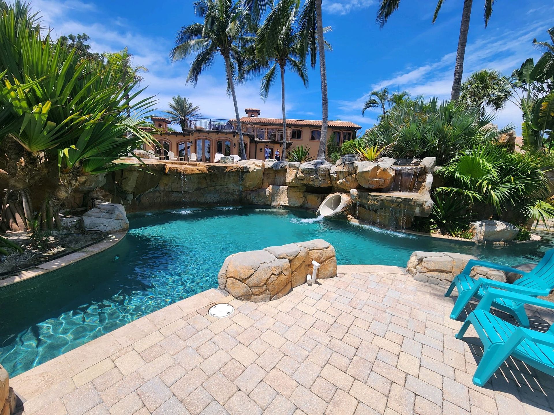 Pool with waterfall feature and a house in the background on a sunny day.