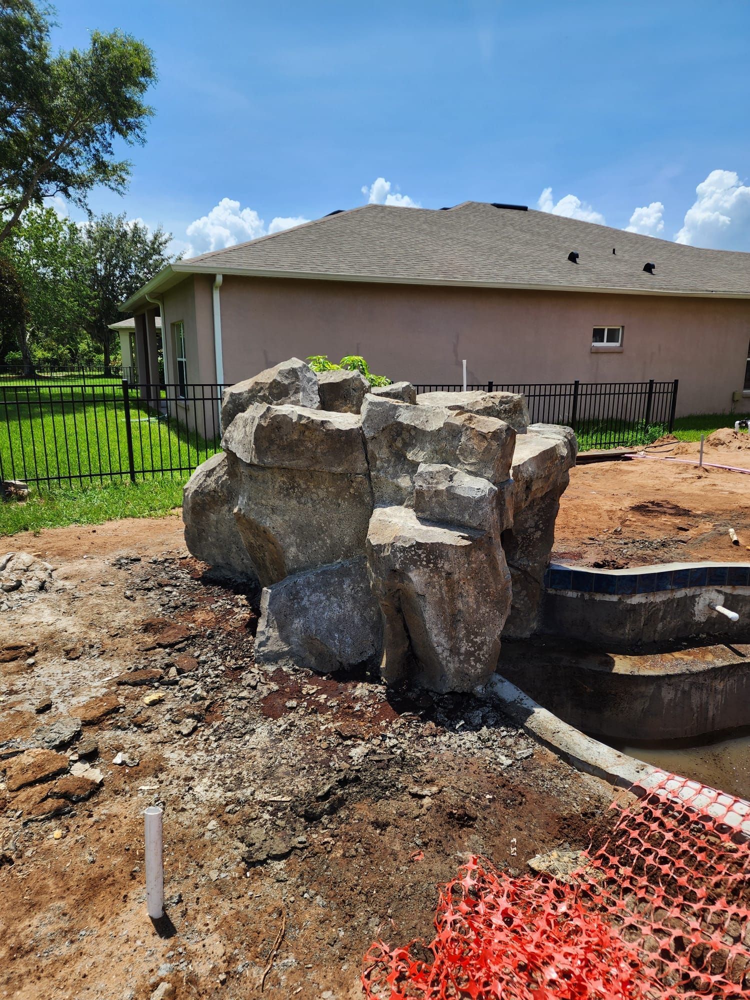 Rock waterfall feature under construction next to a partially built pool. House and fence in background.