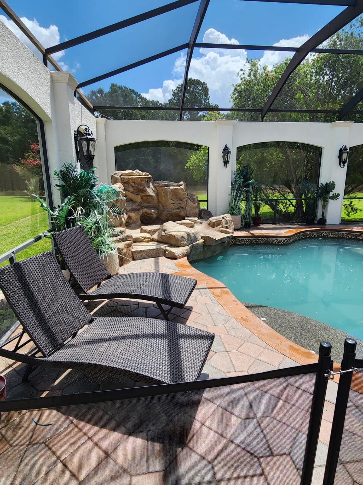 Pool area with lounge chairs, a rock waterfall feature, and a screened enclosure.