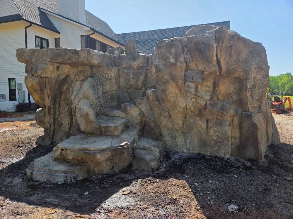 Artificial rock formation with steps, possibly for a pool or landscaping, against a building.