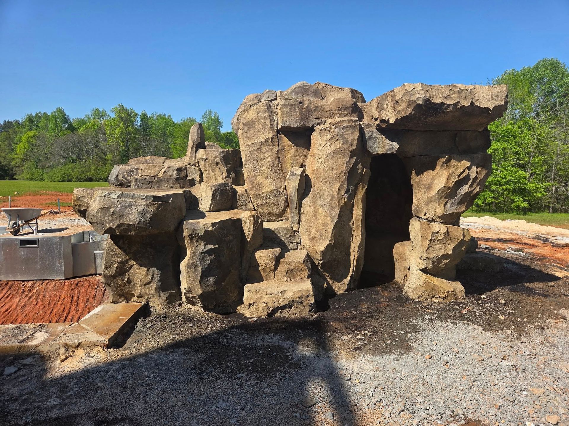 Stone structure resembling a cave entrance in an outdoor setting with red clay and gravel.
