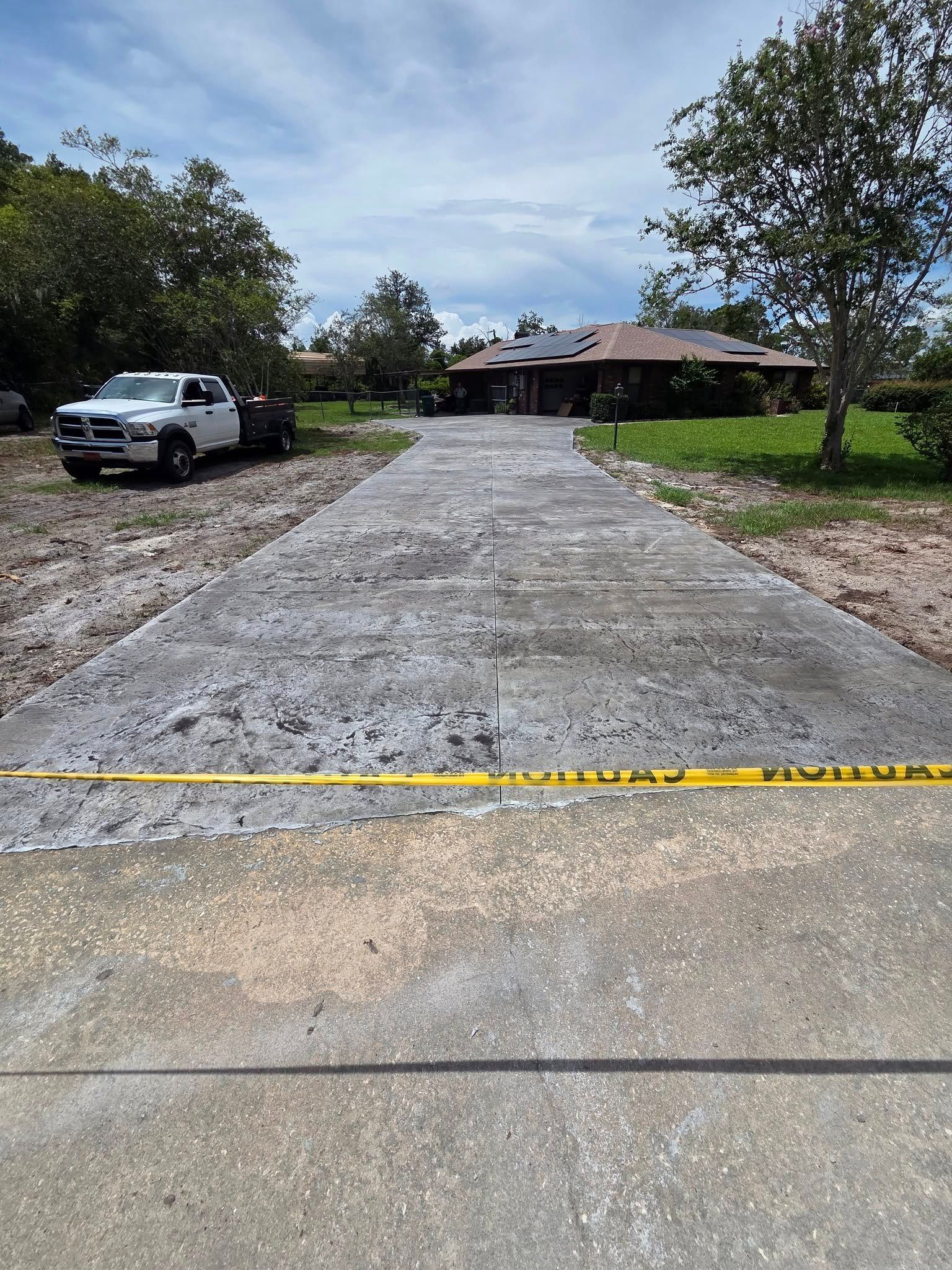 Newly poured concrete driveway leading to a house, with a truck parked on the side. Yellow caution tape is across the driveway.
