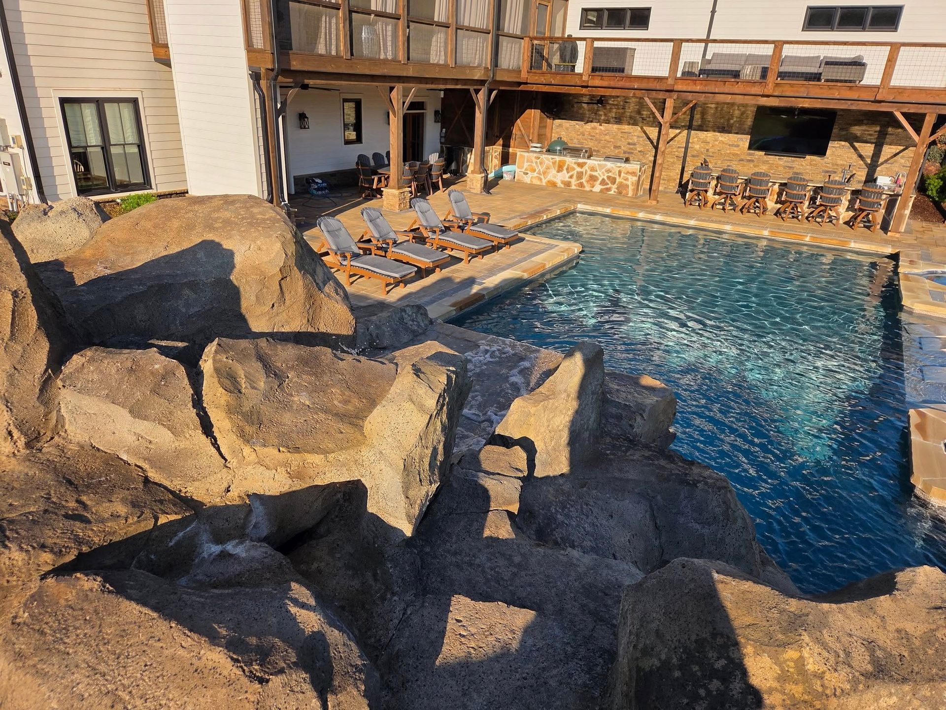 Swimming pool surrounded by rocks and a deck with lounge chairs.