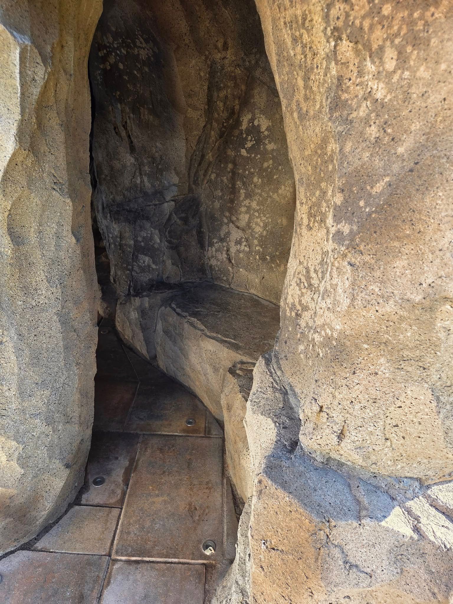 Stone alcove with a built-in stone bench, on a tiled floor. Dark, weathered interior.