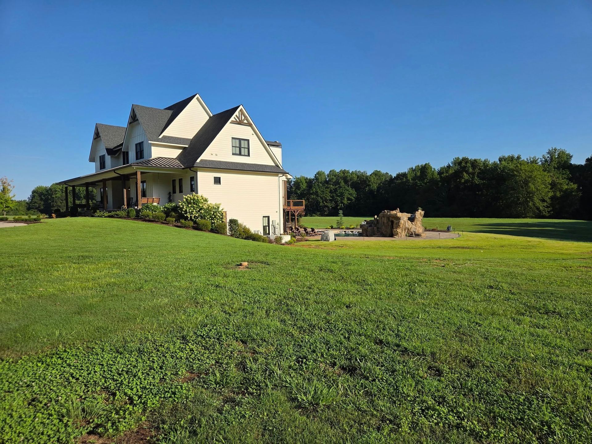 Two-story beige house with dark roof and large yard on a sunny day.