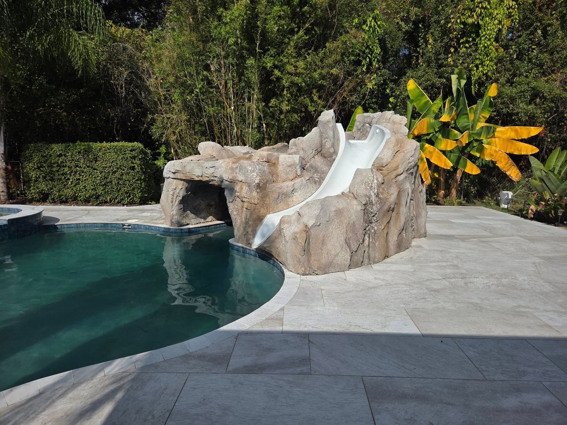 Pool with rock formation water slide. Slide empties into pool, surrounded by stone patio and landscaping.