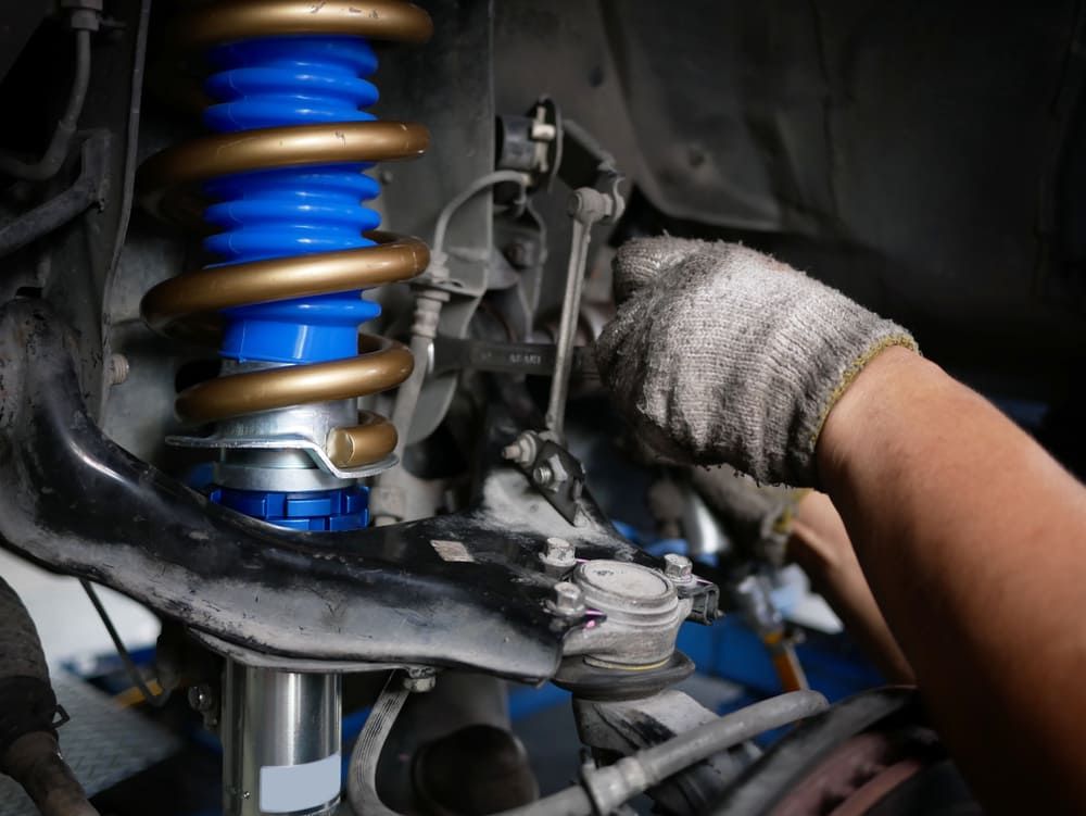 A Person Is Working On A Car Suspension With A Wrench — Vehicle Inspections & Mechanical Services in Albury, NSW
