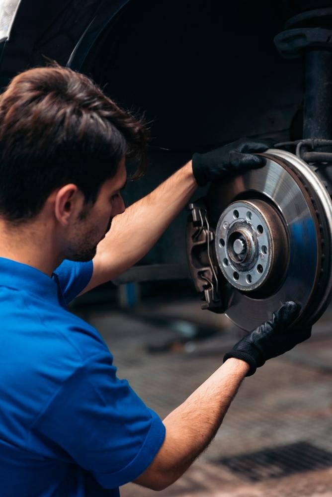 A Man In A Blue Shirt Is Fixing A Brake Disc On A Car — Affordable Mechanic in Albury, NSW