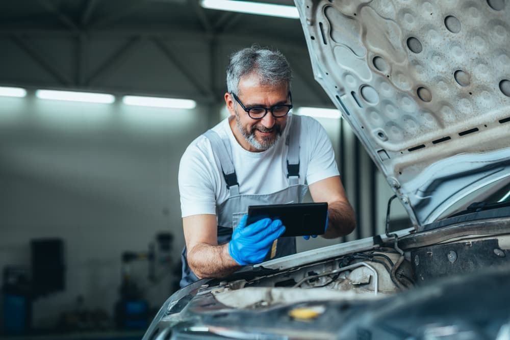 A Man Is Looking At A Tablet While Working On A Car — Book a Vehicle Inspection in Albury, NSW