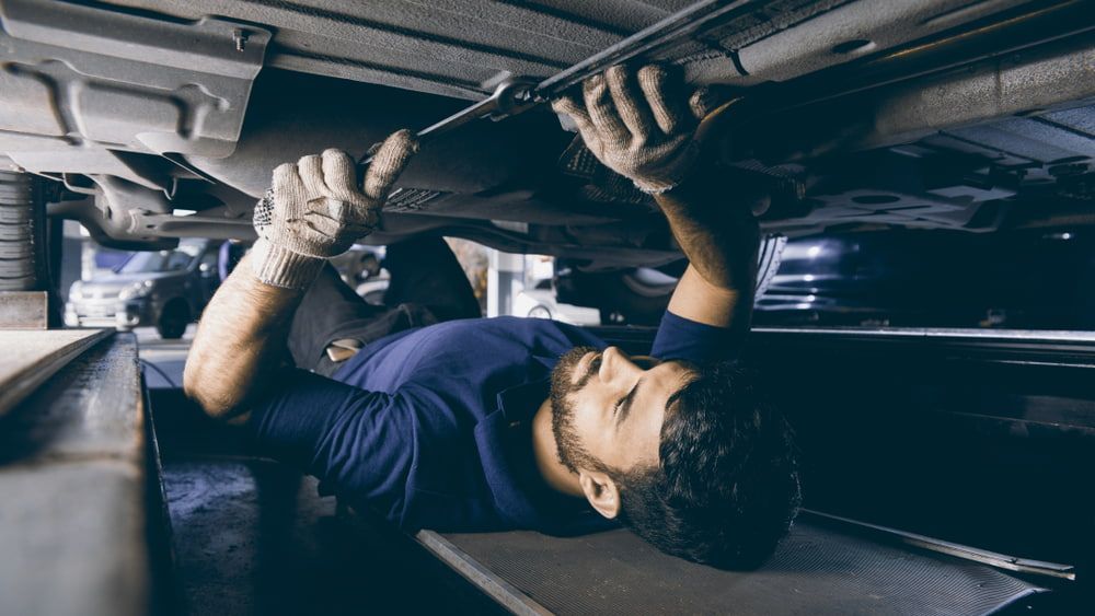 A Man Is Laying On His Back Under A Car In A Garage — Affordable Mechanic in Albury, NSW