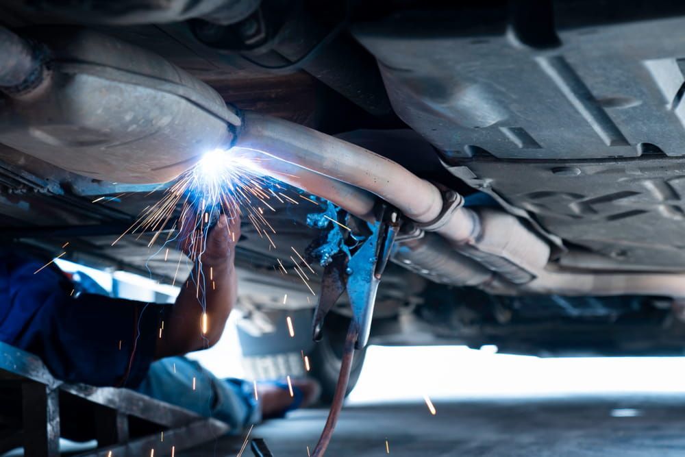 A Man Is Welding The Exhaust Pipe Of A Car — Vehicle Inspections & Mechanical Services in Albury, NSW