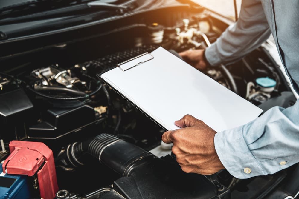 A Man Is Looking Under The Hood Of A Car While Holding A Clipboard — Your Experienced Mechanic in Wodonga, VIC