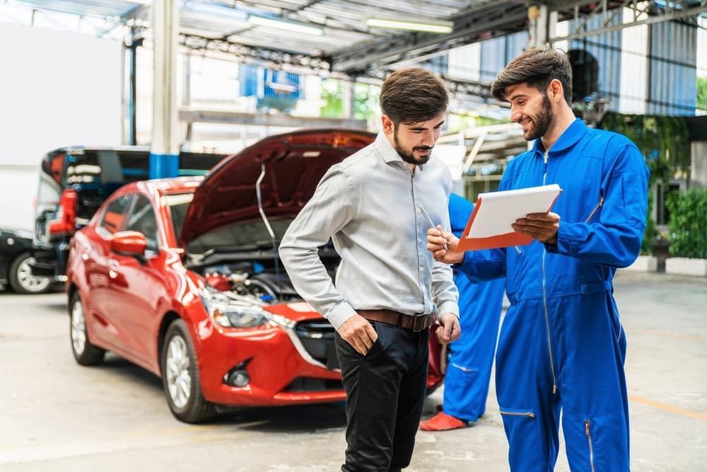 A Man Is Standing In Front Of A Red Car While A Mechanic Looks At A Clipboard — Affordable Mechanic in Albury, NSW