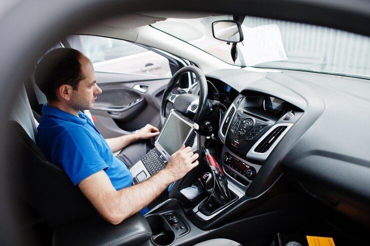 A Man Is Sitting In The Driver 's Seat Of A Car Using A Laptop — Servicing Car Air Conditioning in Albury, NSW