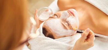 Trattamento viso in una spa con una donna sdraiata, ricoperta di crema bianca che viene applicata con un pennello.