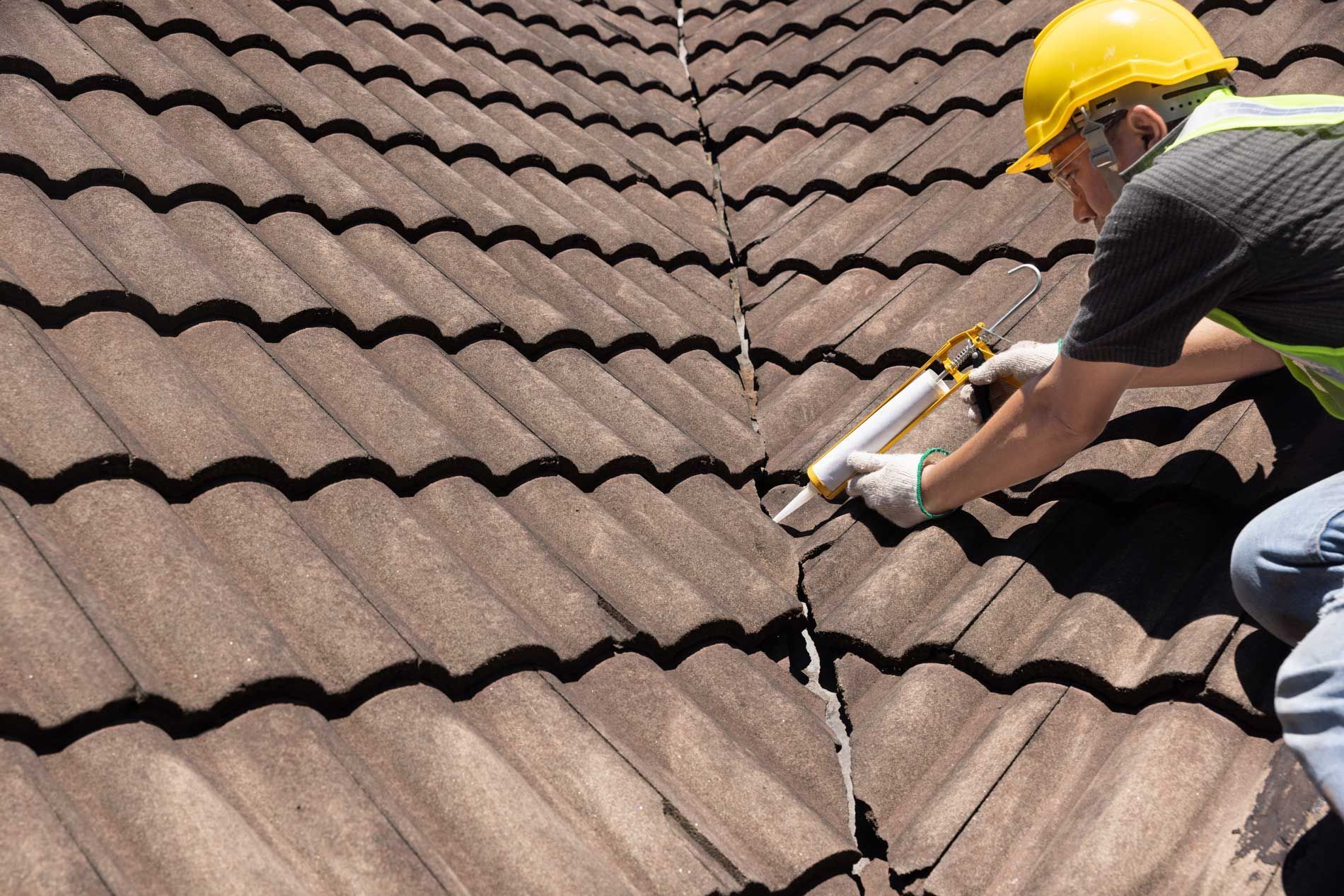 A roofer applying silicone sealant to repair a cracked roof tile. A roofer applying silicone sealant to repair a cracked roof tile.