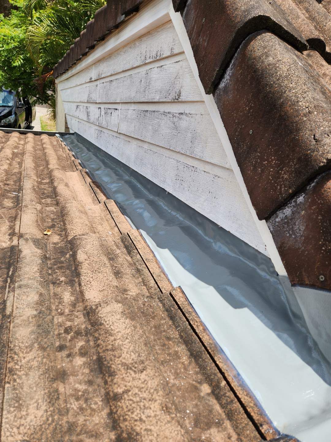 A gray metal valley flashing installed on a pitched tile roof adjacent to white siding.