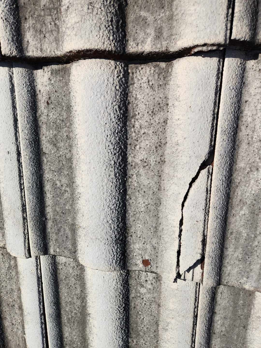 A close-up view of textured, gray concrete roof tiles showing a horizontal crack and a vertical break in one tile.