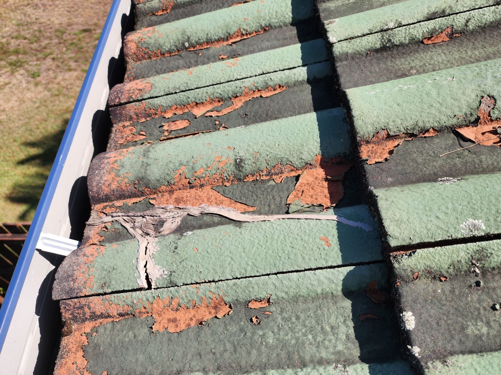 A section of an old, weathered green tiled roof with significant peeling paint and a visible crack in a tile.
