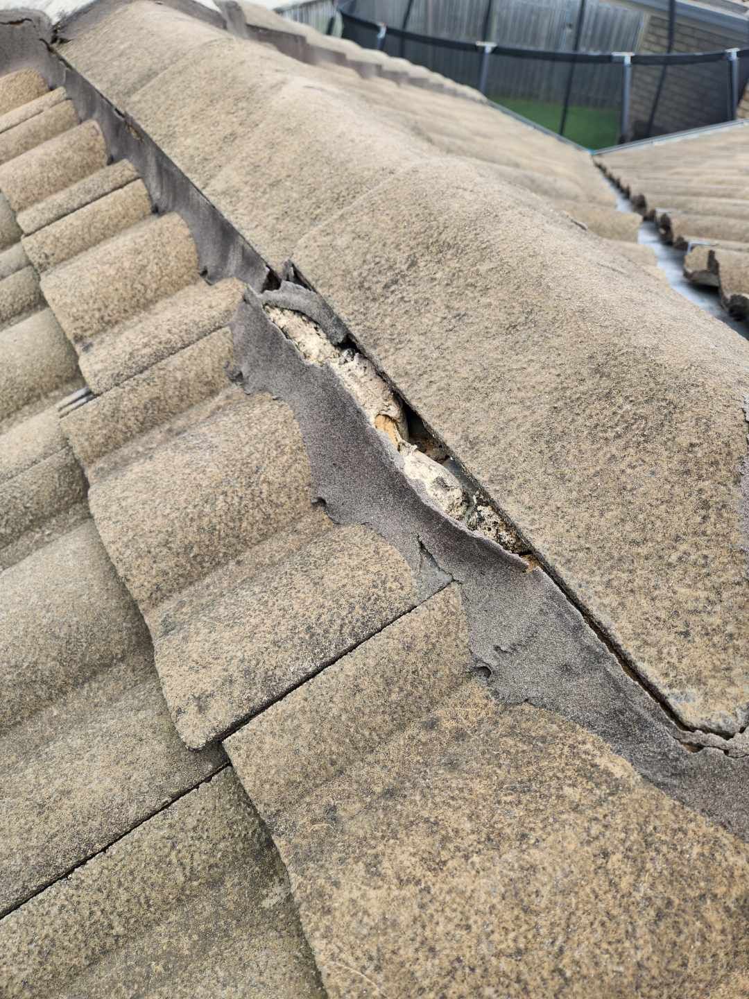 Damaged ridge cap tiles on a roof with visible mortar gaps and cracked bedding material.