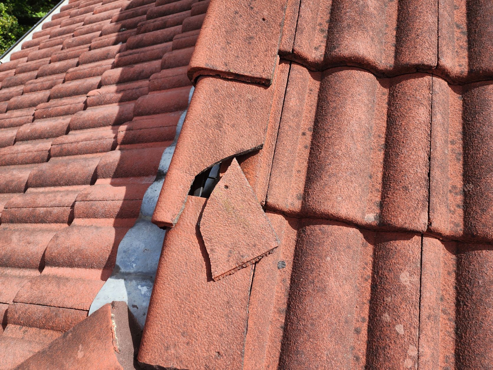 Close-up of a damaged red concrete roof tile with a broken piece shifted out of place.