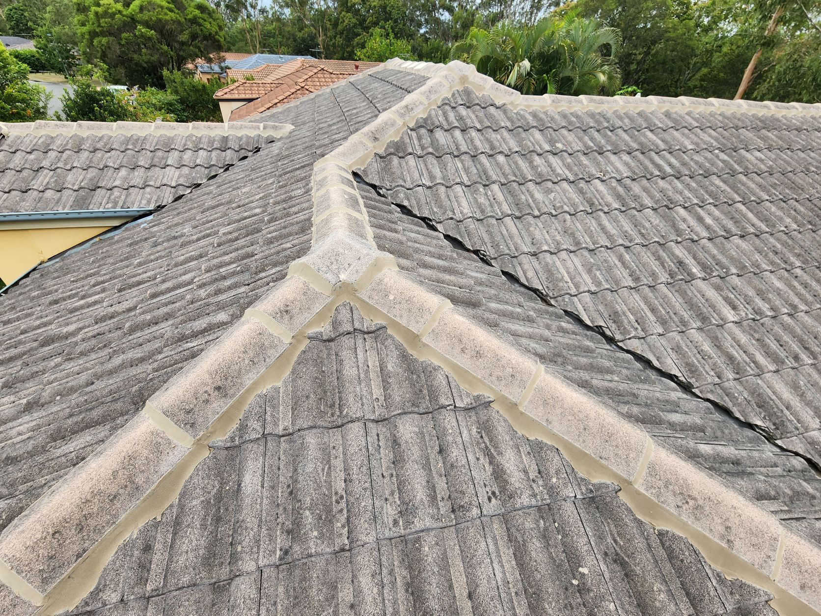 A close-up view of a grey concrete tile roof with weathered ridges and visible mortar lines.