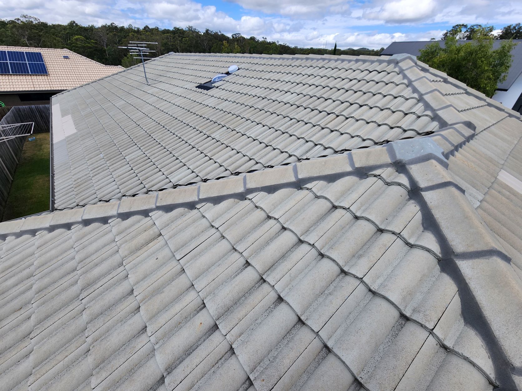 High-angle view of a tiled residential roof featuring grey concrete tiles, a central ridge, and a small rooftop vent.