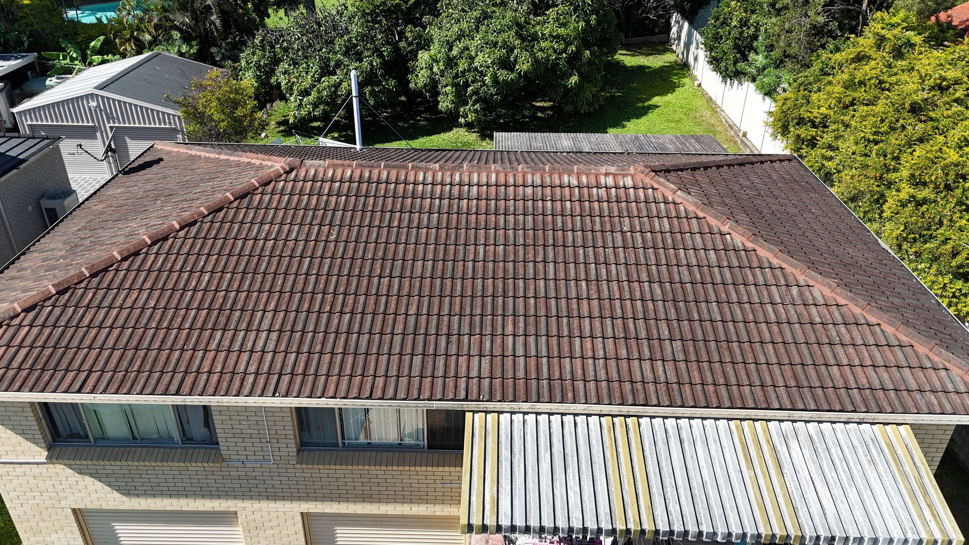 Aerial view of a brown tiled roof on a two-story brick house with a white slat awning over the garage area.