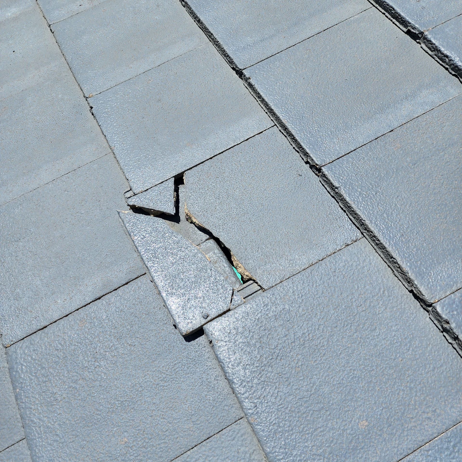 A cracked, grey stone paver among intact square tiles on a paved surface.