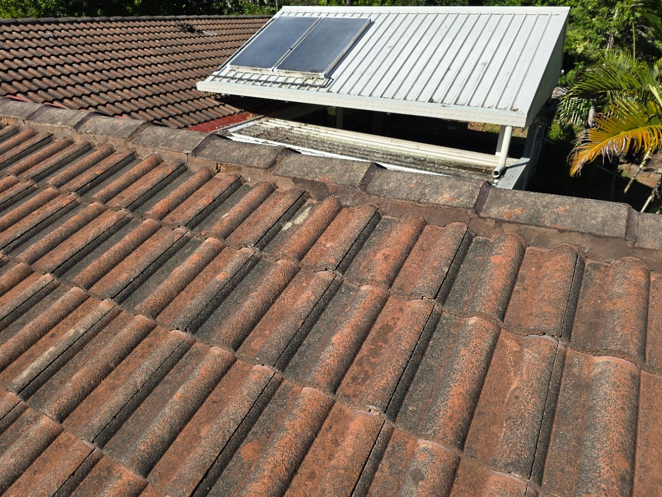 Close-up of two roofs with faded terracotta tiles. A metal patio roof with solar panels is visible.