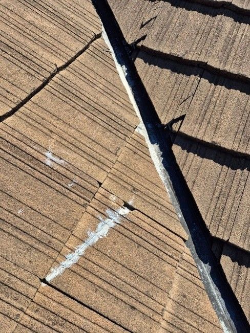 Close-up of two sections of a roof. There's a visible crack and white residue along the ridge.