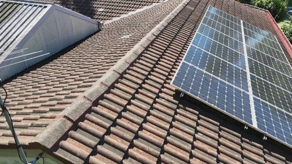 Close-up of a roof with clay tiles, partially covered by solar panels.