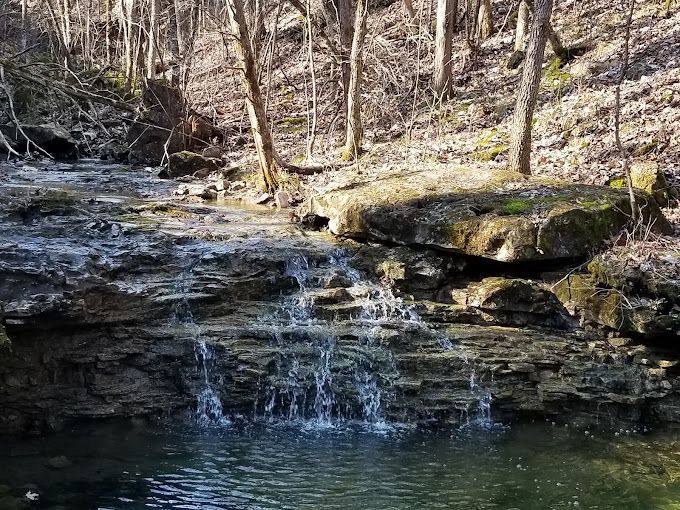 A small waterfall is surrounded by rocks and trees in the woods.