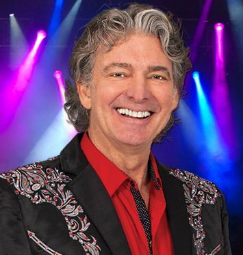A man wearing a red shirt and a black jacket is smiling