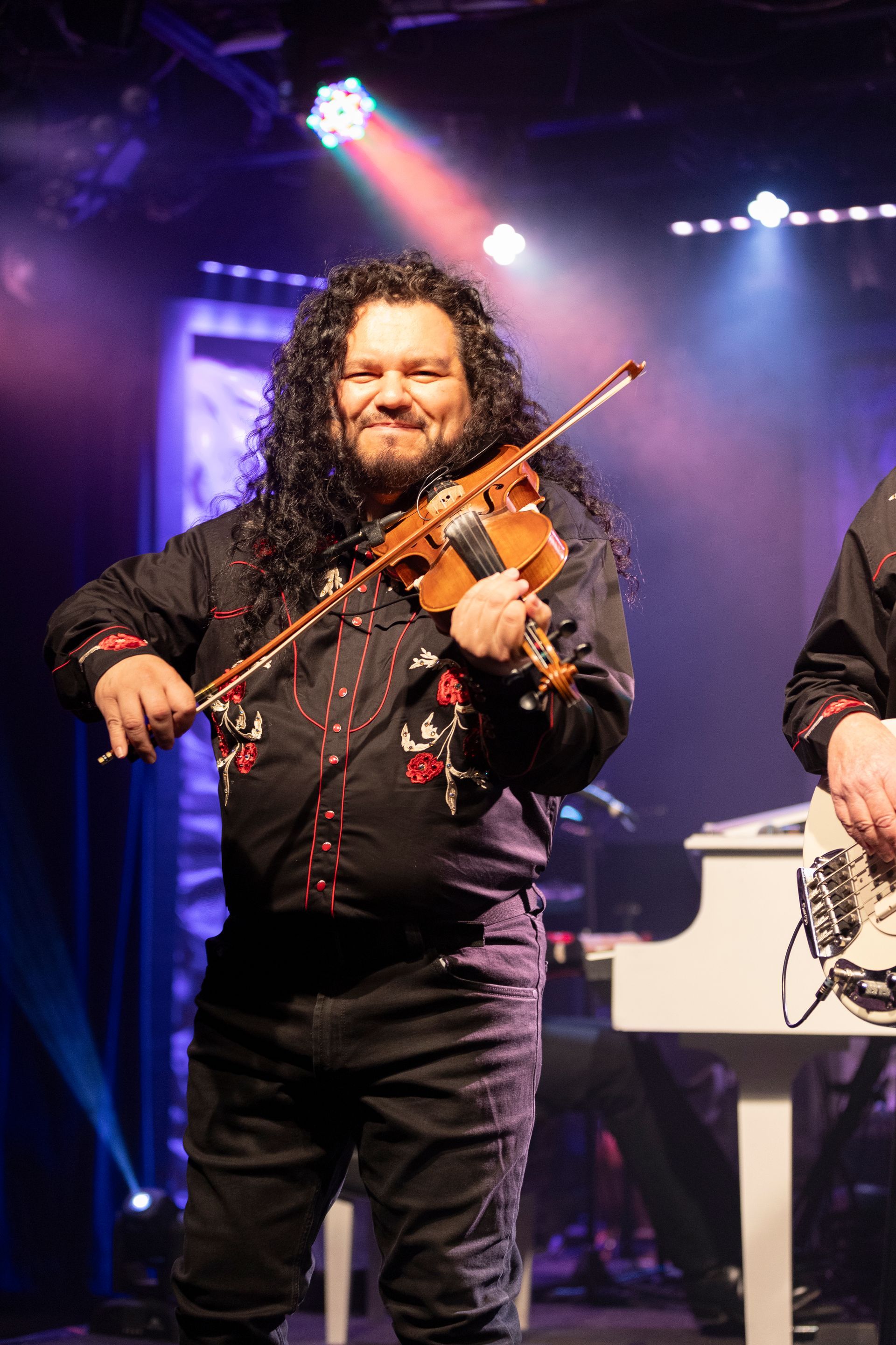 A man with long hair is playing a violin on a stage.