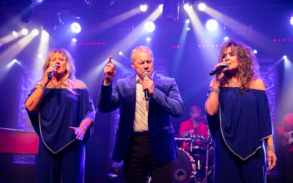 A man and two women are singing into microphones on a stage.