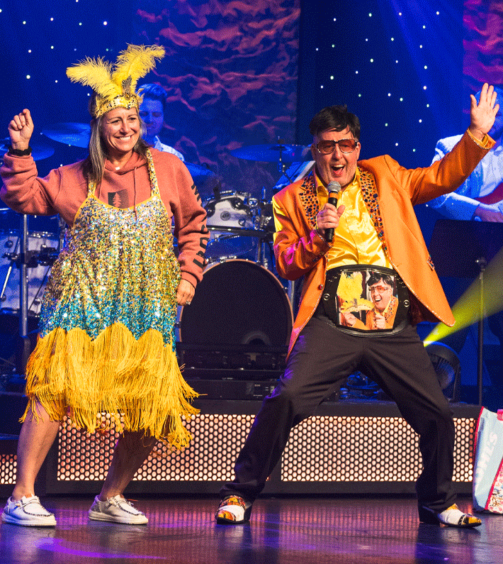 Four men in blue suits singing into microphones on a stage, with a band and the text 