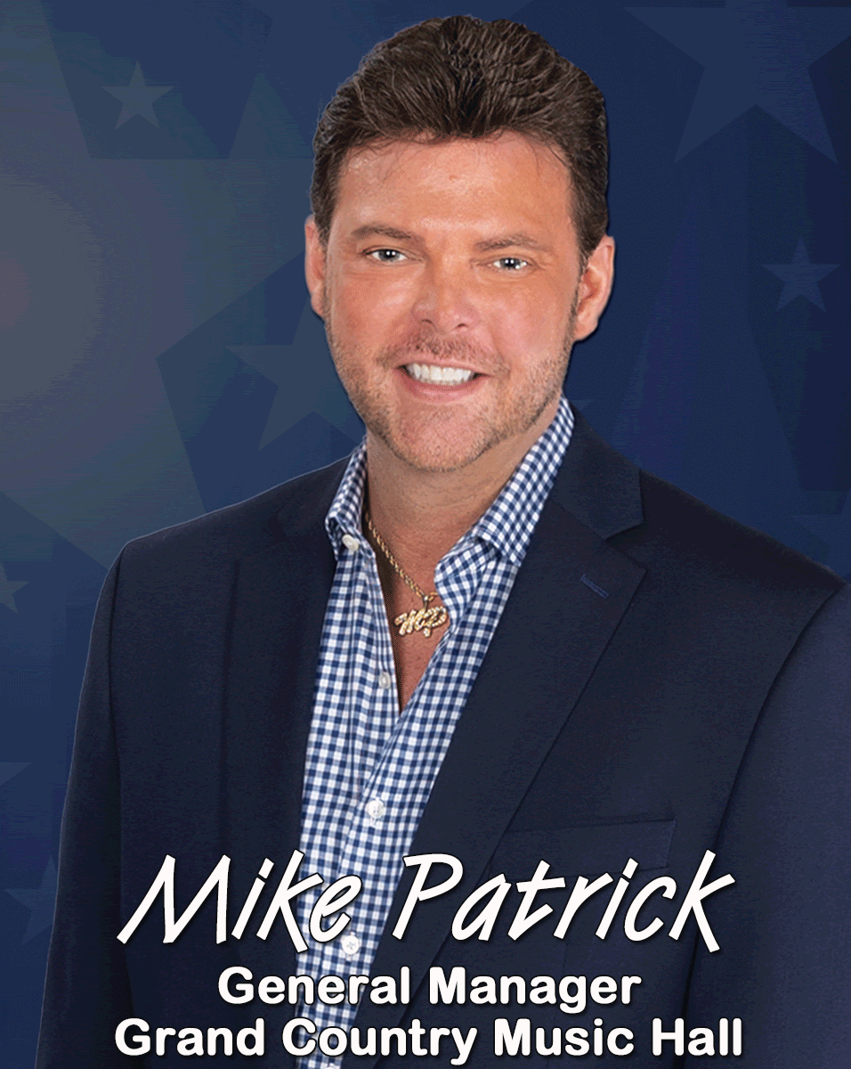 Mike Patrick, General Manager at Grand Country Music Hall, wearing a navy blazer and checkered shirt against a blue background.