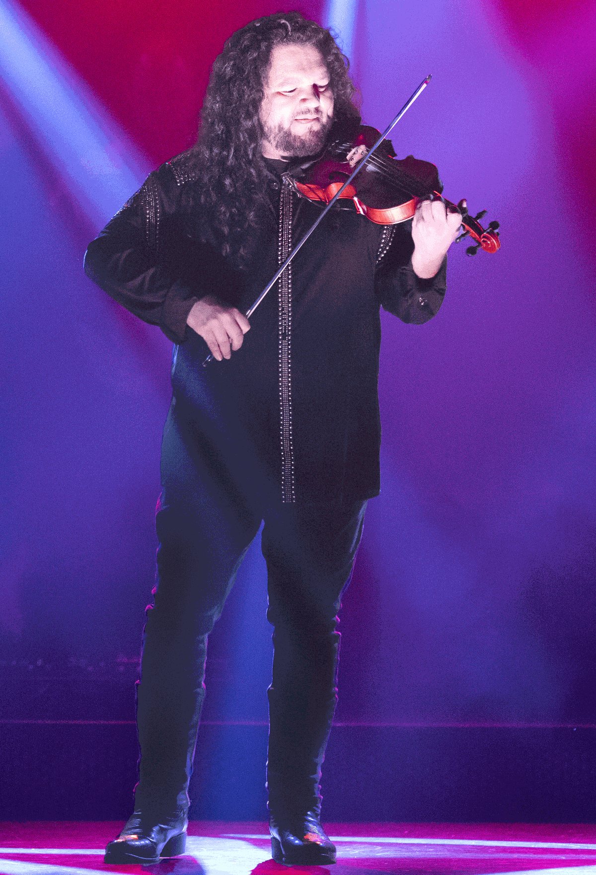 Smiling musician playing a red electric guitar on a purple-lit stage