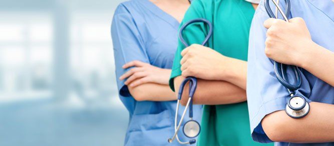 Two healthcare workers in blue scrubs with stethoscopes, standing with arms crossed in a clinic setting