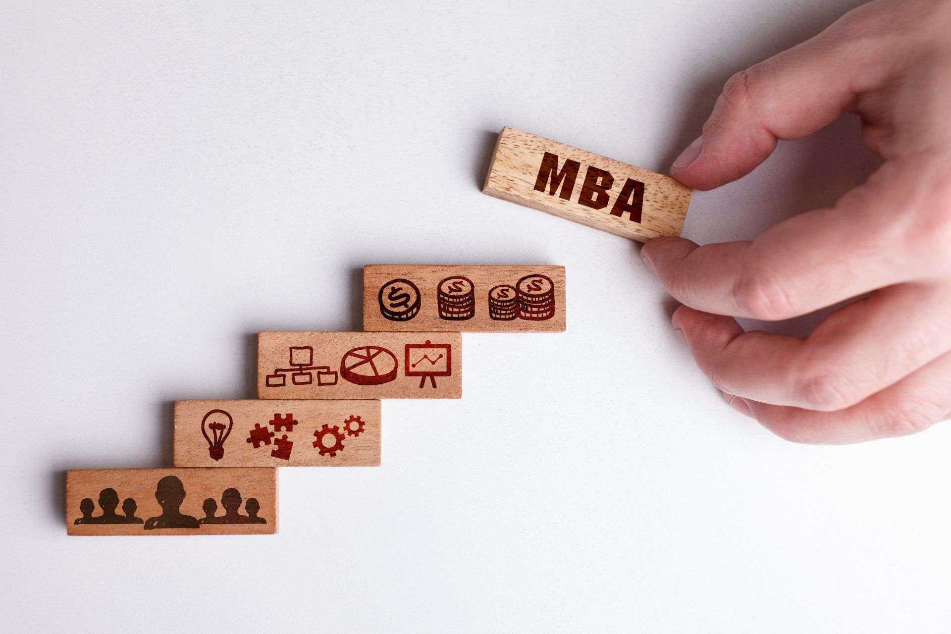 Hand placing an MBA block above a staircase of wooden career-growth icons
